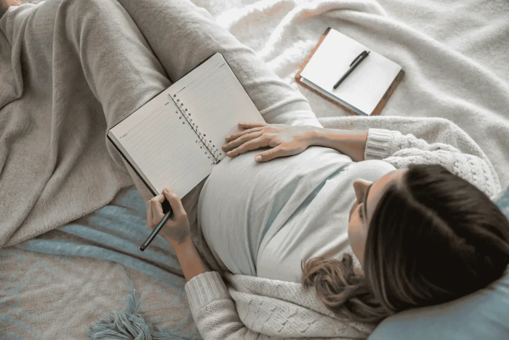 A person connecting with their body, hands on heart and womb, with their manifestation journal resting beside them during a somatic ritual.