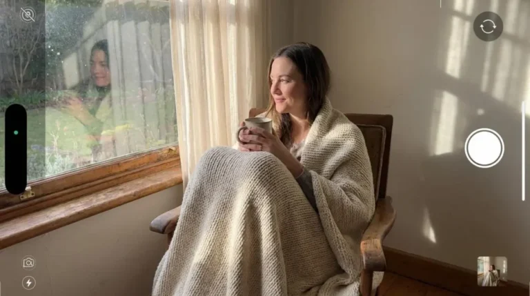 Woman wrapped in a cream weighted blanket by a sunlit window for functional freeze recovery.